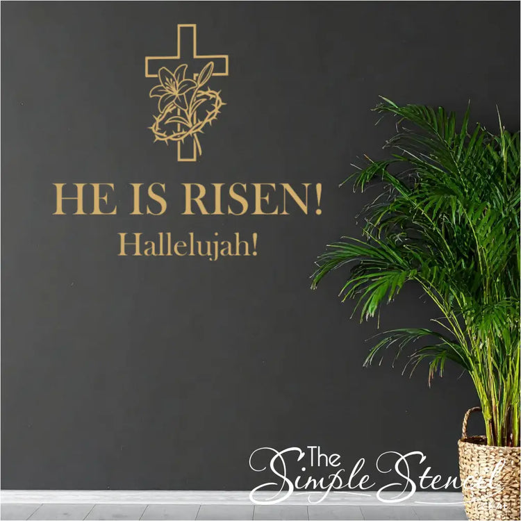 Premium metallic gold 'He Is Risen!' wall lettering with the resurrection cross graphic, applied to a dramatic matte black accent wall next to a large potted palm.