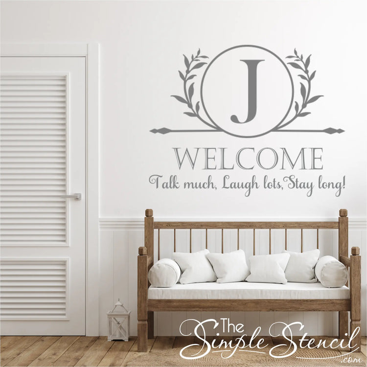Wooden bench with white cushions against a wall with large rotunda monogram decal and decorative text and letter 'J' design.