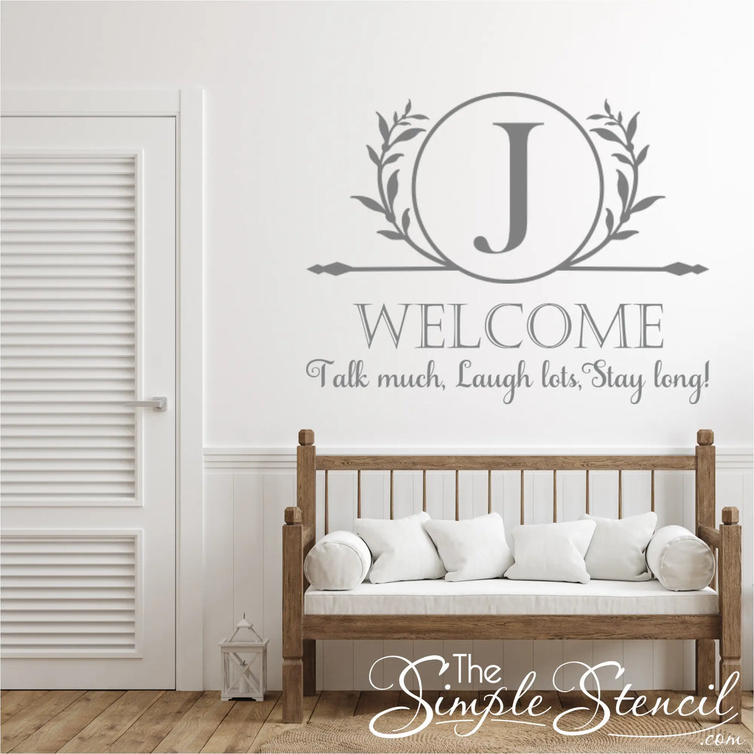 Wooden bench with white cushions against a wall with large rotunda monogram decal and decorative text and letter 'J' design.