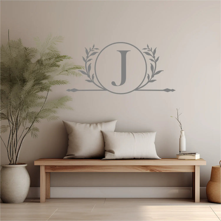 Decorative wall decal with a monogram 'J' in a wreath above a wooden bench with pillows.