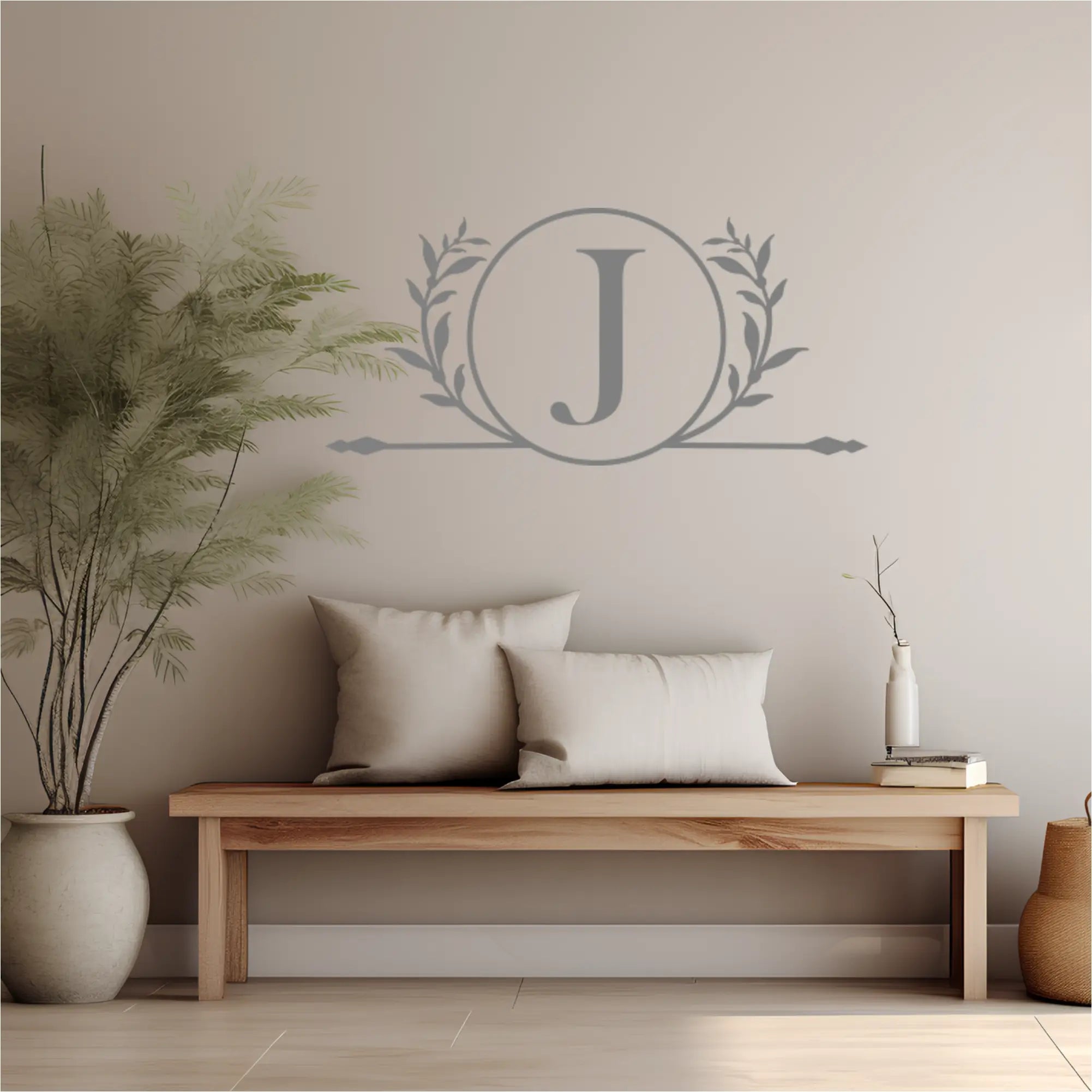 Decorative wall decal with a monogram 'J' in a wreath above a wooden bench with pillows.