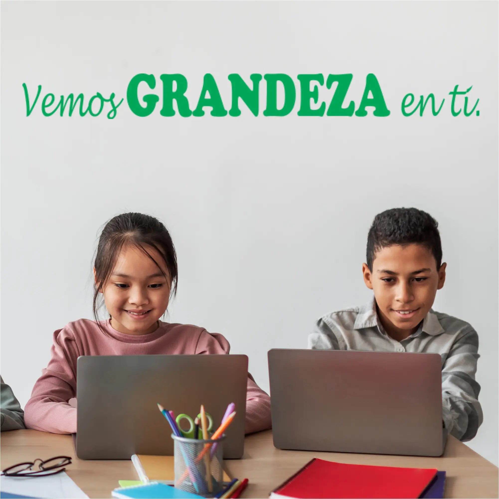 Two children using laptops at a desk beneath a vemos grandeza spanish version school wall decal