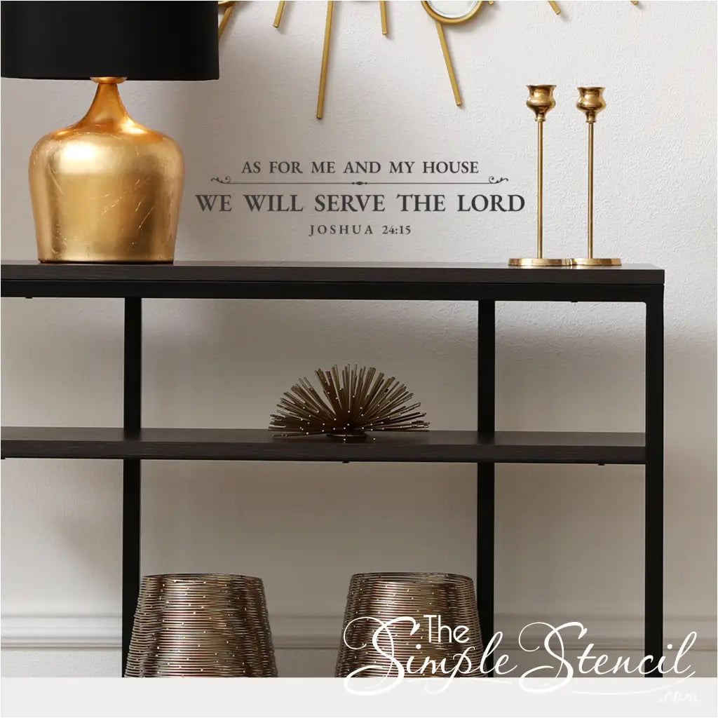 Elegant gold wall decal of "As For Me and My House, We Will Serve the Lord" Joshua 24:15 centered on a white wall above a modern black console table with gold lamps and decor.
