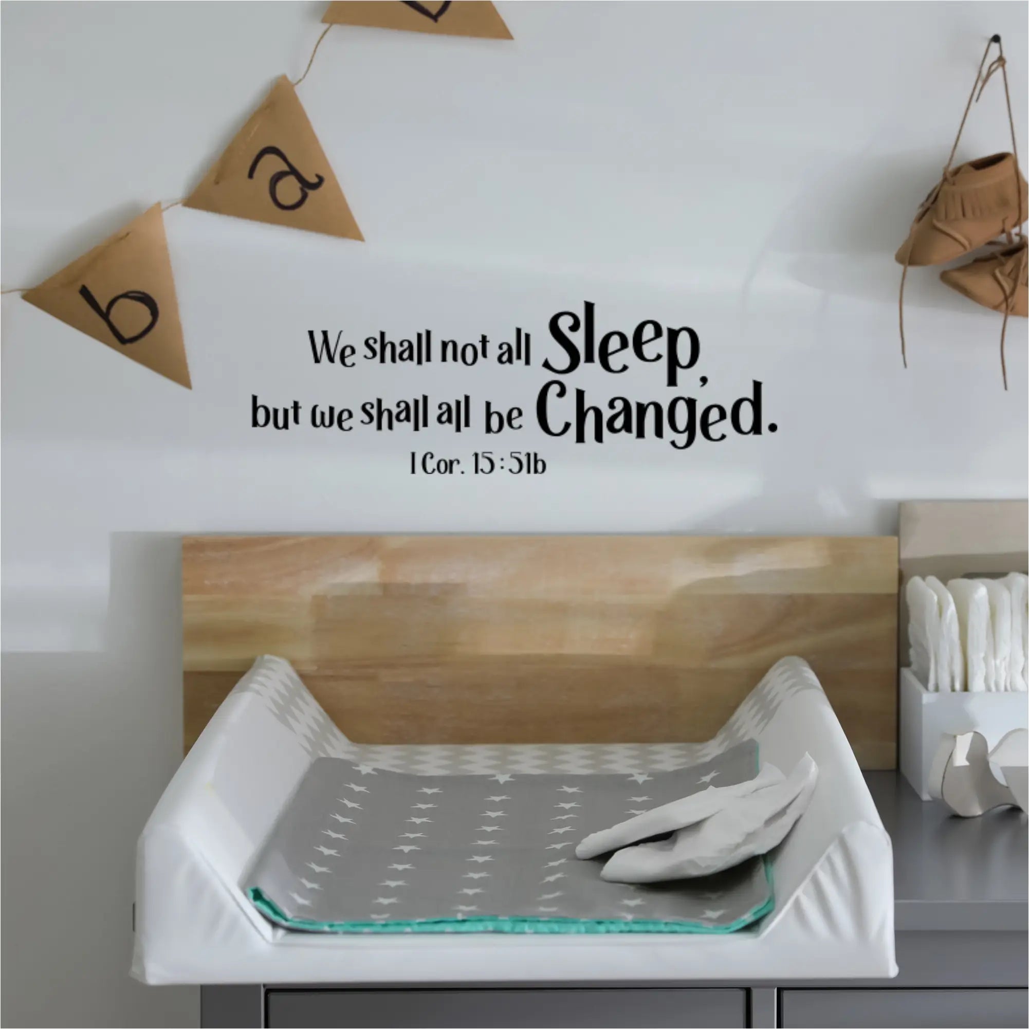 A humorous and thought-provoking wall decal reading "We shall not all sleep, but we shall all be changed. 1 Cor. 15:51b" positioned above a baby changing table in a nursery.
