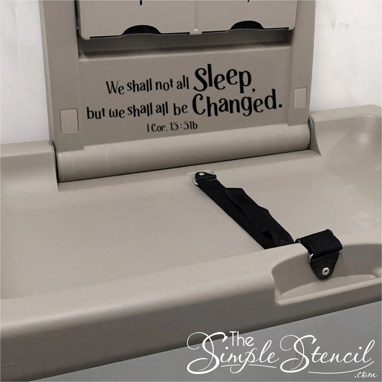 A lighthearted and relatable wall decal featuring "We shall not all sleep, but we shall all be changed. 1 Cor. 15:51b" above a diaper changing station in a church nursery.