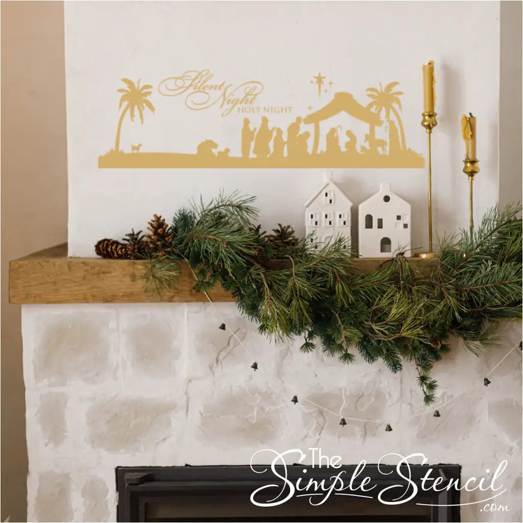 Close-up of a gold Silent Night holy night wall decal placed above a fireplace mantel decorated with pine garland and white ceramic houses. Excellent example of religious holiday wall decor and Christmas vinyl lettering on a rustic mantle.
