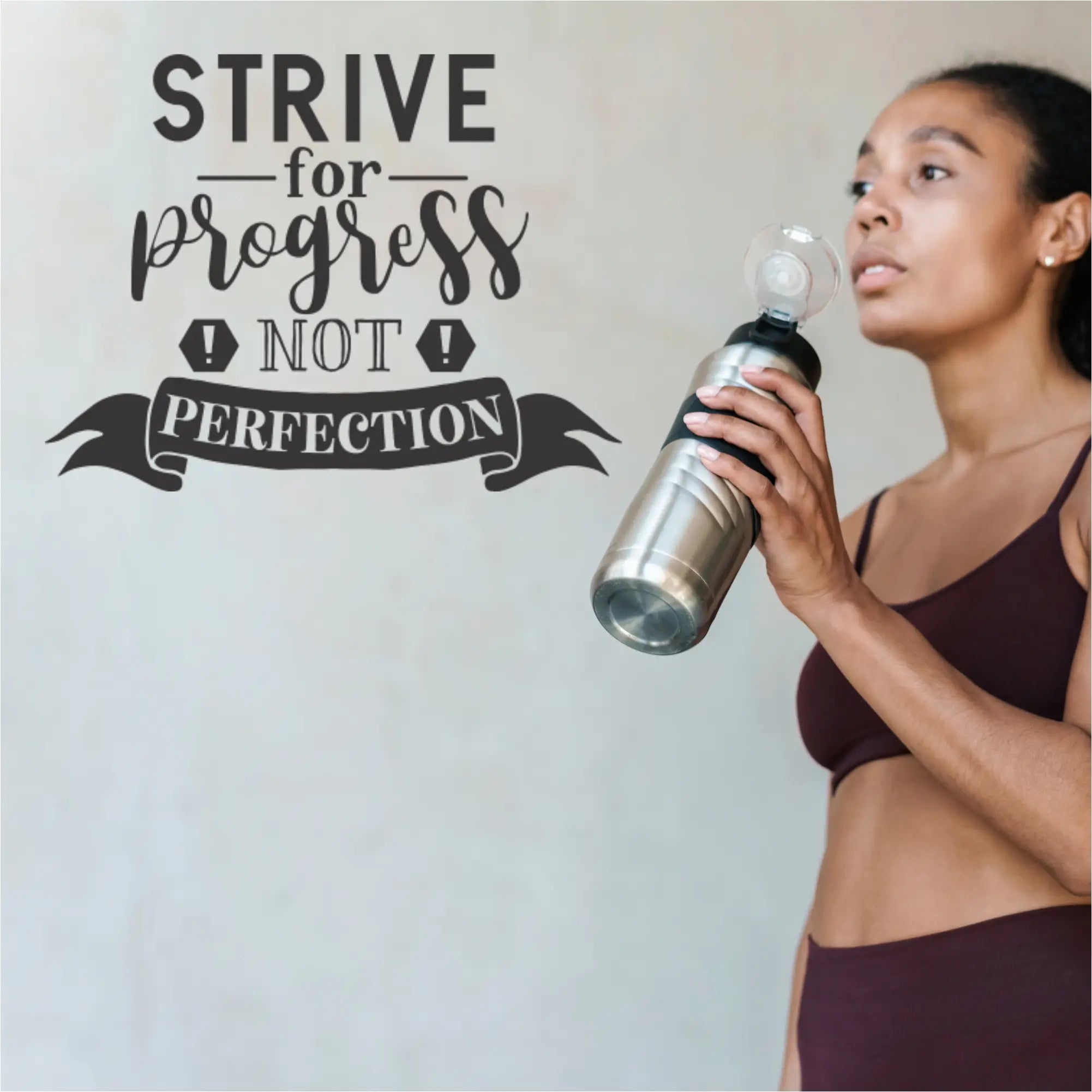 Woman holding a water bottle with motivational quote decal on a light gray gym wall