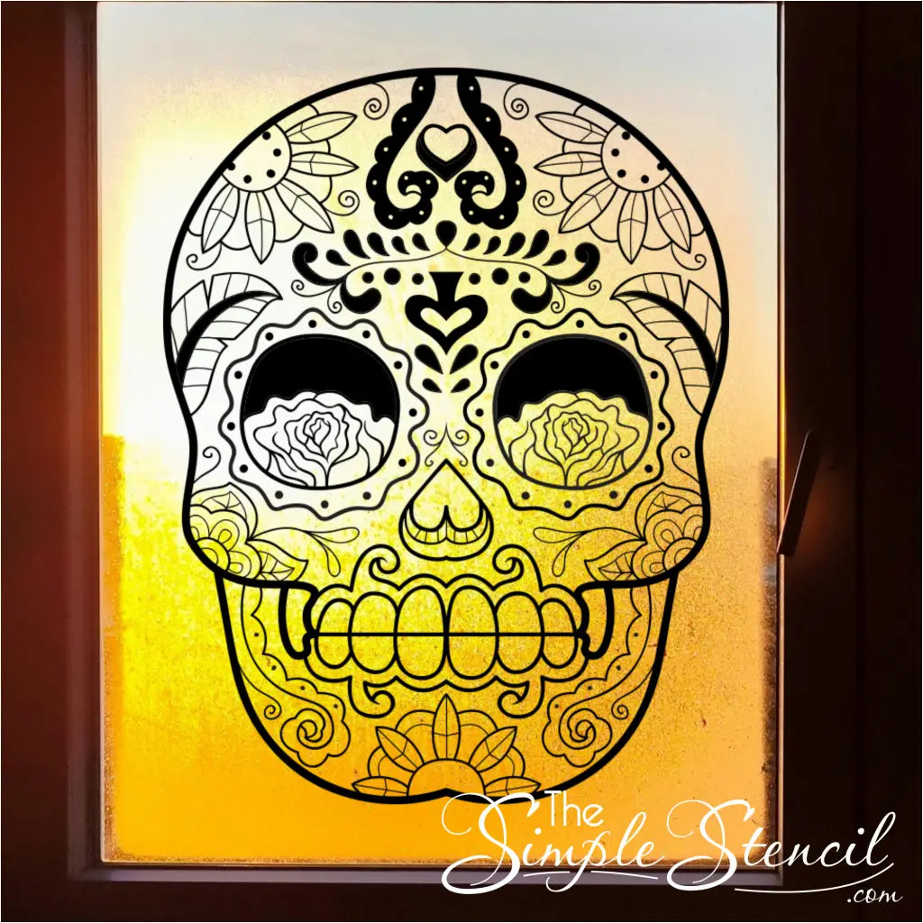 A black sugar skull vinyl decal applied to a window, with a bright, sunny background shining through the design. - By The Simple Stencil shown in 22" x 28.5"size in Matte Black