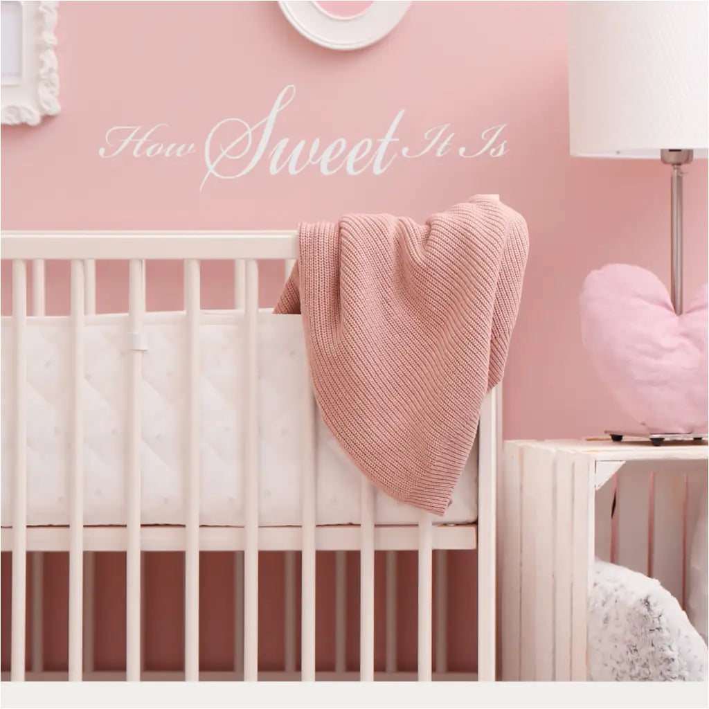 "How Sweet It Is" wall decal in white on a colorful pink nursery wall over a crib. 