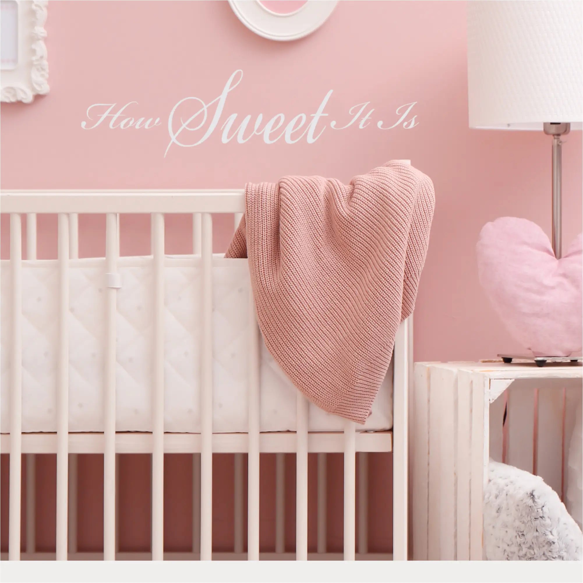 "How Sweet It Is" wall decal in white on a colorful pink nursery wall over a crib. 