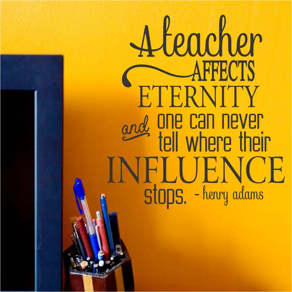 A vinyl wall decal with black text on a light-colored background: "A teacher affects eternity and one can never tell where their influence stops. ~Henry Adams" Displayed over a teacher's office desk area. By The Simple Stencil