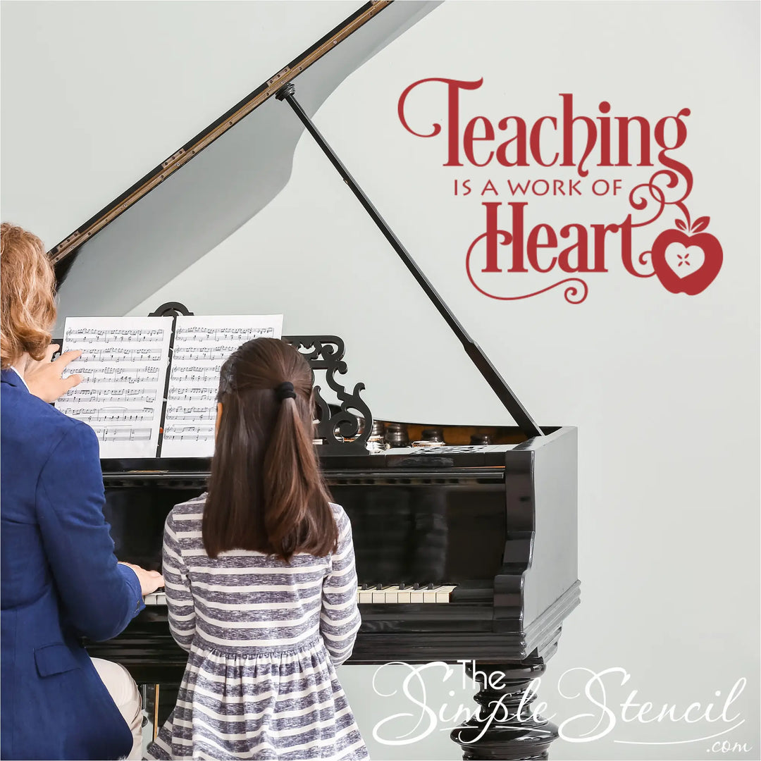 A sophisticated, light-filled piano studio with a grand piano. A music teacher in a blue blazer sits with a young student in a striped dress at the keys. Applied to the warm cream wall above them is a large burgundy vinyl decal reading 'Teaching is a Work of Heart' in elegant script. The overall lighting is bright and premium.