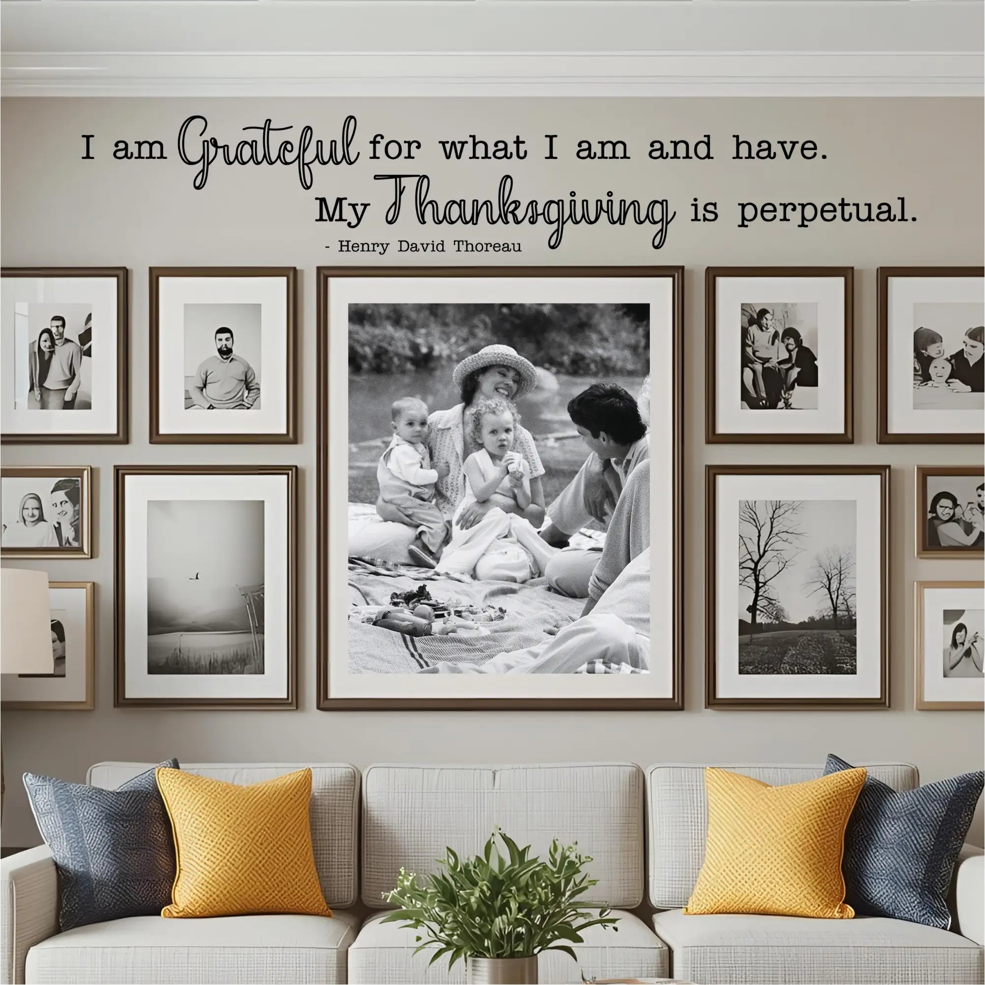 A living room with a cozy sofa and a large gallery wall of black and white family photos. The "I am grateful for what I am and have..." wall decal is placed as a central, guiding piece of art for the entire photo collection, highlighting its use in creating a permanent, gratitude-focused display.