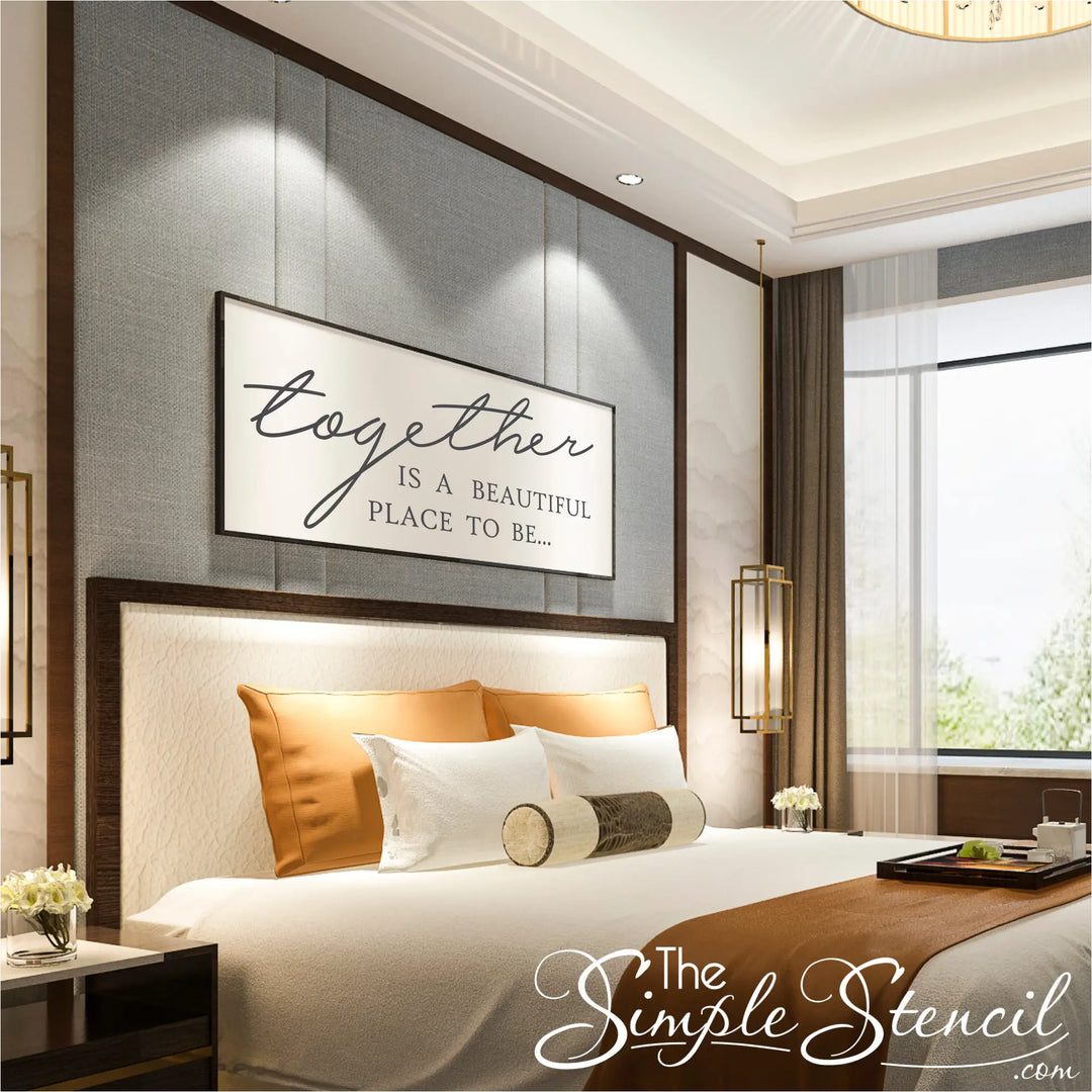 A large white horizontal picture frame above a luxury bed featuring a black "Together is a beautiful place to be" vinyl sticker, creating a sophisticated framed art look.