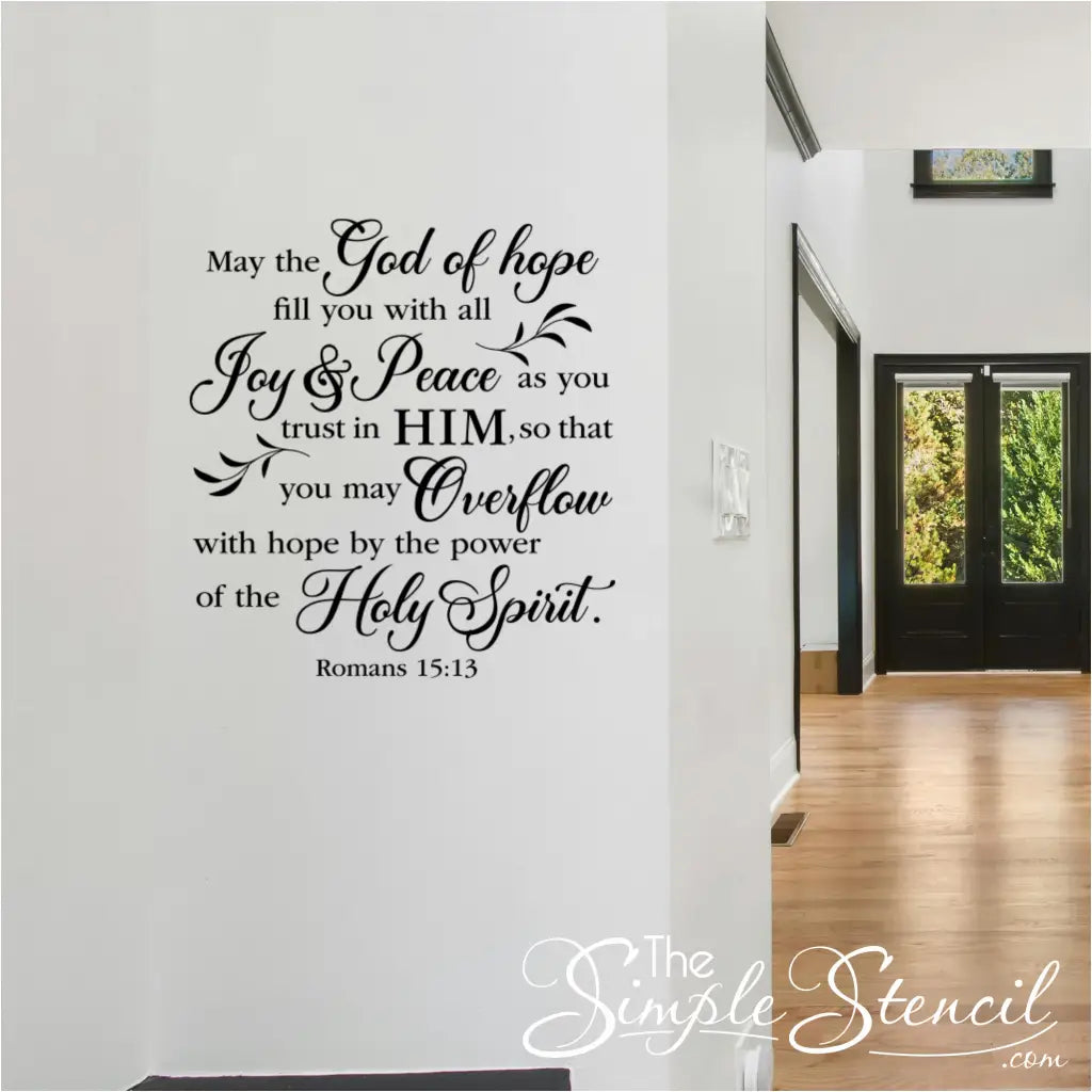 Large, black vinyl wall decal in an elegant script and serif font on a white hallway wall reading "May the God of hope fill you with all Joy & Peace... Romans 15:13."