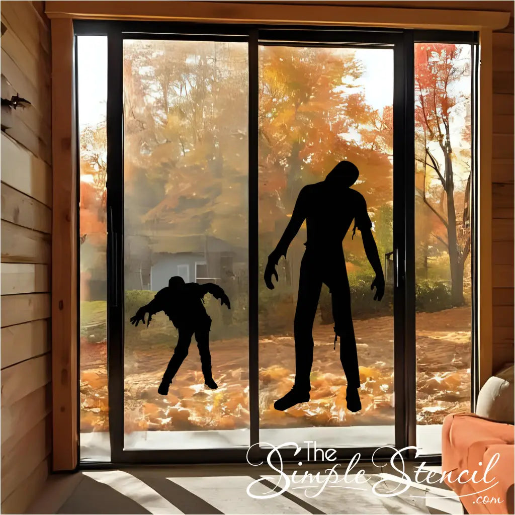 A black walking zombie silhouette vinyl decal on a sliding glass door, with an autumn forest in the background.