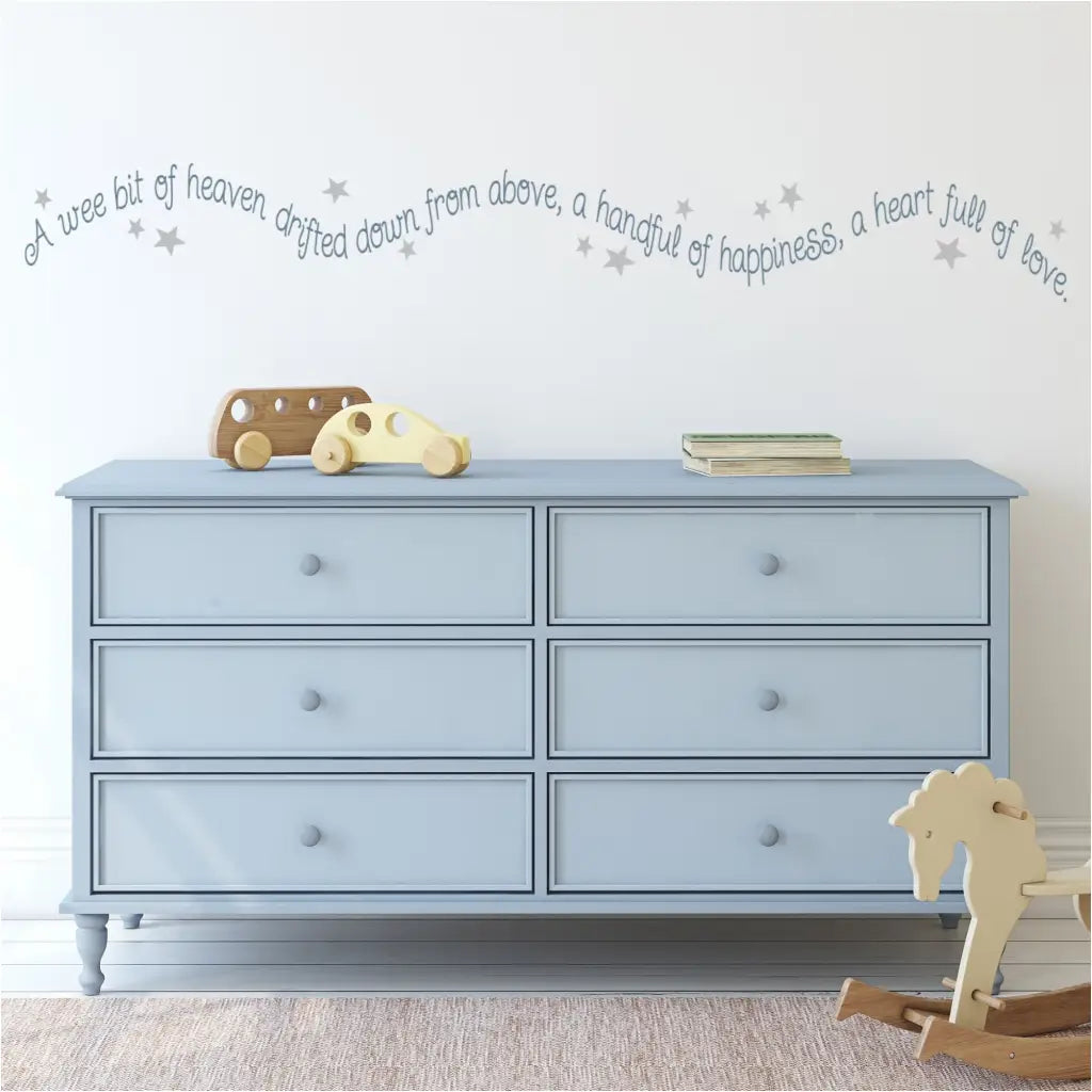 An adorable wall quote decal for a baby nursery in a wavy pattern with stars by The Simple Stencil. Reads: A wee bit of heaven drifted down from above, a handful of happiness, a heart full of love. 
