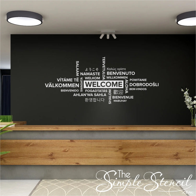 A wide-angle shot of a modern office entryway featuring a large wall decal with the phrase 'Welcome' written in a multitude of languages. 