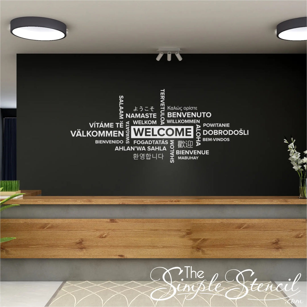 A wide-angle shot of a modern office entryway featuring a large wall decal with the phrase 'Welcome' written in a multitude of languages. 