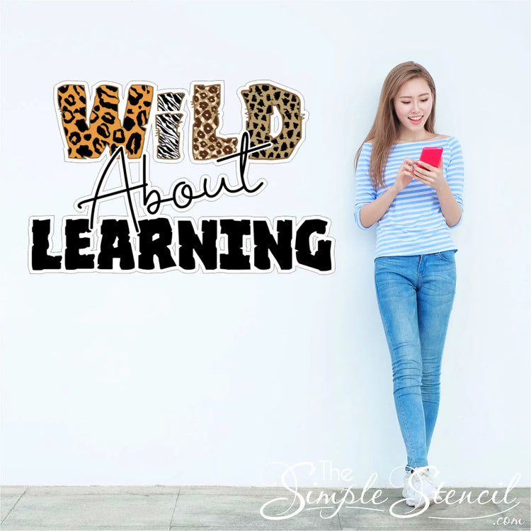 A woman holding a red smartphone wears a striped top near a wild about learning learning wall decal for classroom decor
