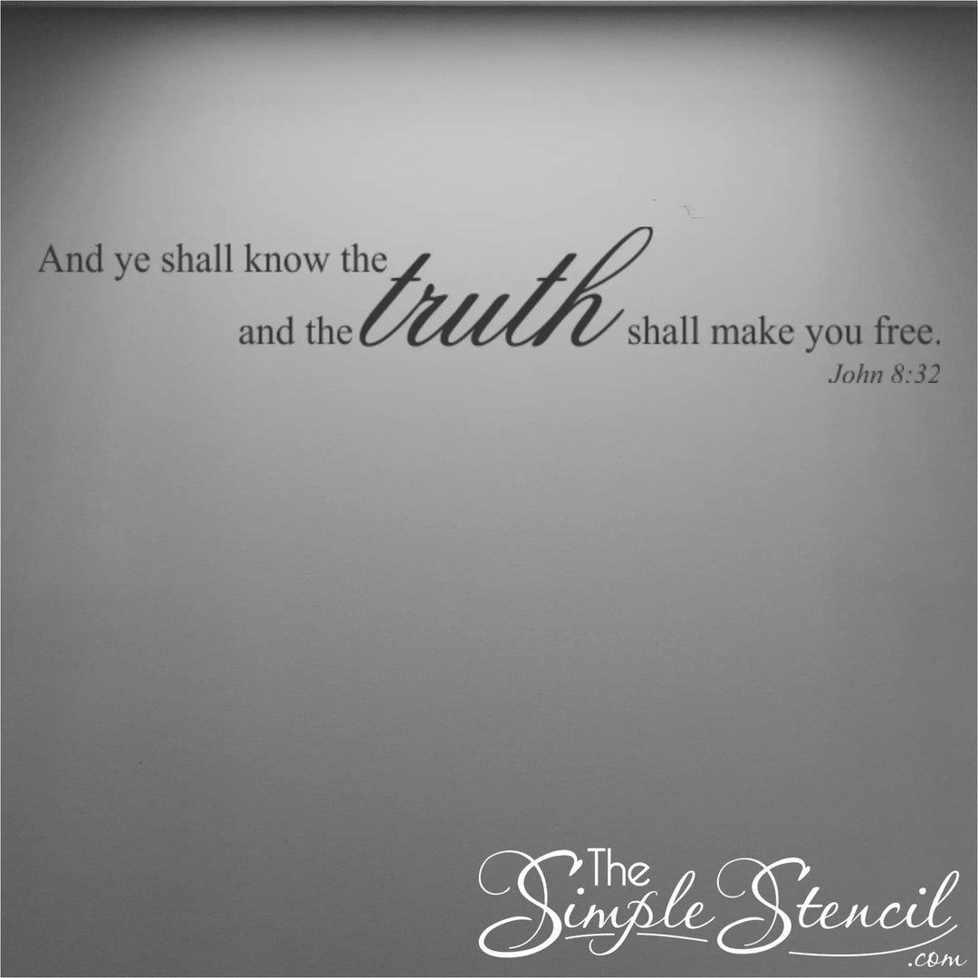 Black vinyl Bible verse decal on a minimalist gray wall with overhead spotlighting, highlighting the elegant mix of serif and script typography.