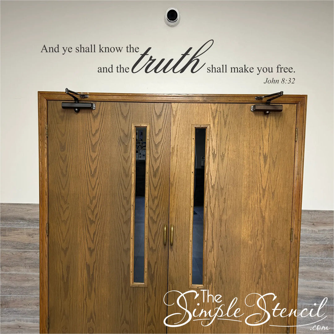 A customer-supplied photo of the John 8:32 scripture decal, 'And ye shall know the truth and the truth shall make you free,' installed in black vinyl on a white wall directly above a set of double wooden church doors.