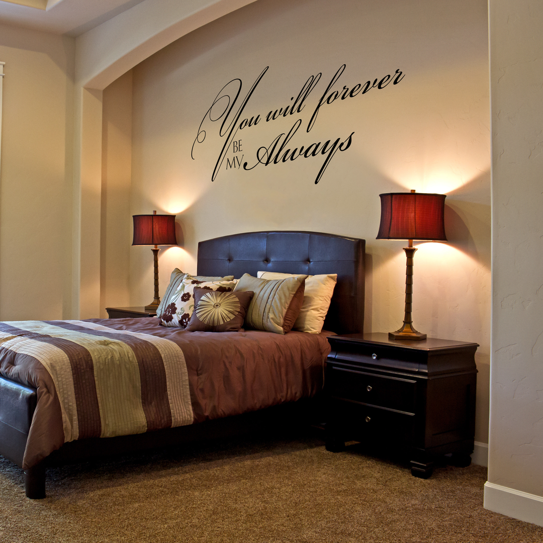 Elegant black vinyl wall decal with the quote "You will forever be my always" in a fancy script font, displayed on a beige wall above a dark leather tufted headboard and matching bedside lamps.