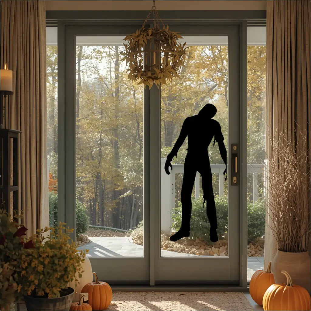 A black zombie silhouette vinyl decal on a large sliding glass door, with a vibrant autumn outdoor scene visible, perfect for Halloween decoration.