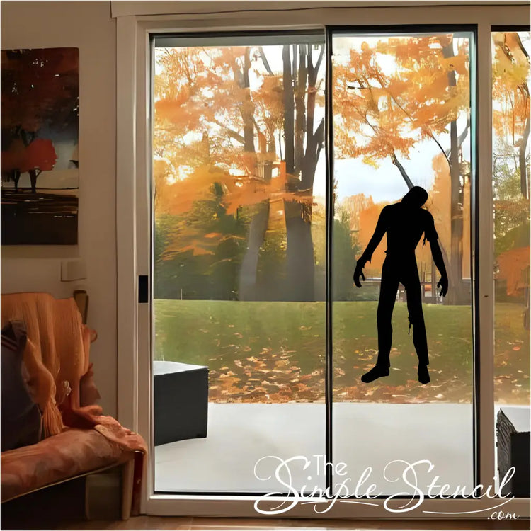 A black zombie silhouette vinyl decal on a large glass window framed by warm wood, showcasing an autumn outdoor view, ideal for Halloween.